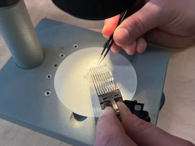 Detail čtecích hlav pevného disku pod lupou s pinzetou